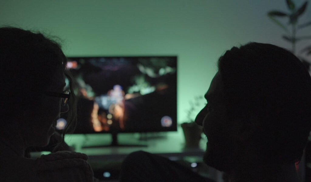 Homem e mulher de perfil em pouca luz com ecrã ou monitor para jogos no meio