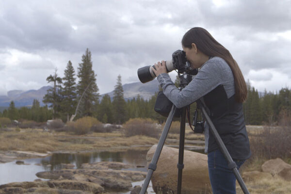 Rapariga a fotografar paisagem com câmara e tripé num mundo da fotografia profissional