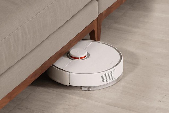 Aspirador robot no chão meio debaixo de um sofá